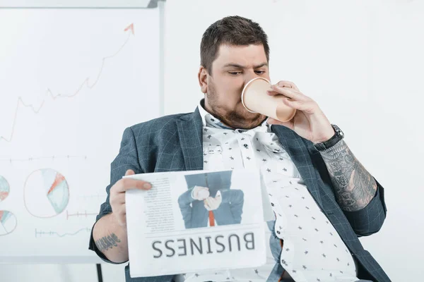 Fat businessman drinking coffee and reading business newspaper in office — Stock Photo