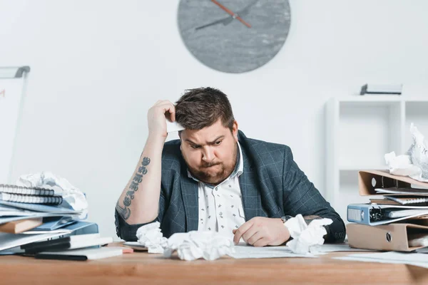 Confuso hombre de negocios con sobrepeso en traje trabajando con documentos en la oficina - foto de stock