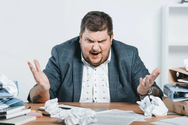 Wütender übergewichtiger Geschäftsmann im Anzug arbeitet mit Dokumenten im Büro — Stockfoto