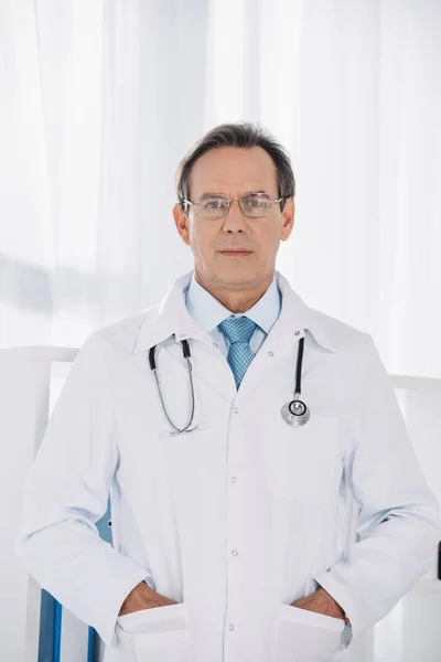 Doctor standing with hands in pockets and looking at camera — Stock Photo