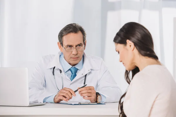 Male serious doctor and female patient sitting at talking at clinic — Stock Photo