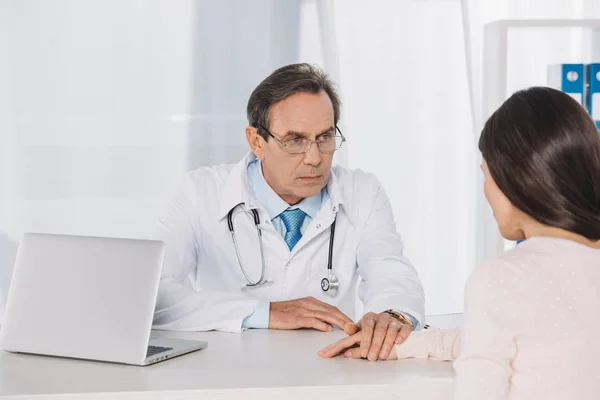 Médico y paciente mujer tomados de la mano en la clínica - foto de stock