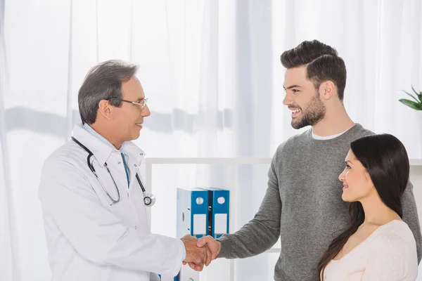 Médico y paciente sonriente estrechando las manos - foto de stock