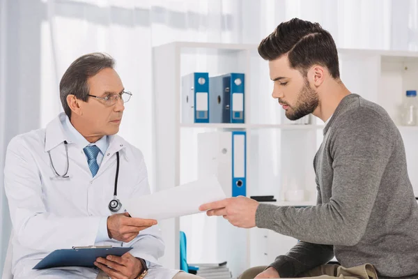 Médico dando documentos para paciente do sexo masculino — Fotografia de Stock