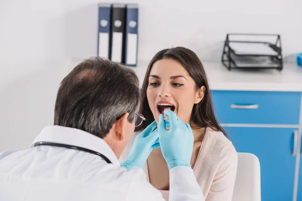 Médico examinando mujer paciente garganta en guantes médicos - foto de stock
