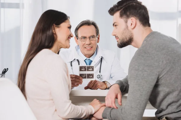 Doctor showing photo of ultrasound diagnostics to happy couple — Stock Photo