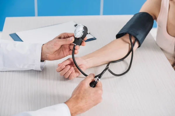 Imagen recortada del médico que mide la presión del paciente femenino - foto de stock