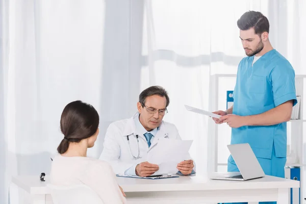 Médico leyendo documentos de pacientes femeninos en la clínica - foto de stock