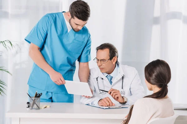 Enfermera masculina mostrando algo al médico en la tableta - foto de stock