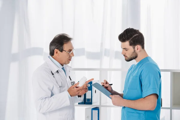 Médico sosteniendo pastillas y hablando con la enfermera - foto de stock