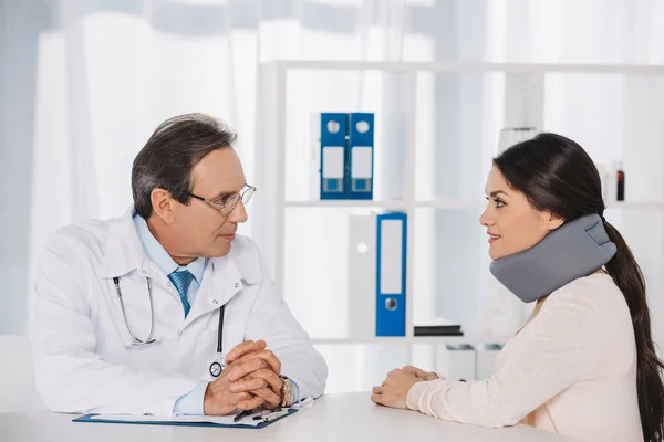 Доктор сидит и разговаривает с пациенткой в шейном корсете — стоковое фото