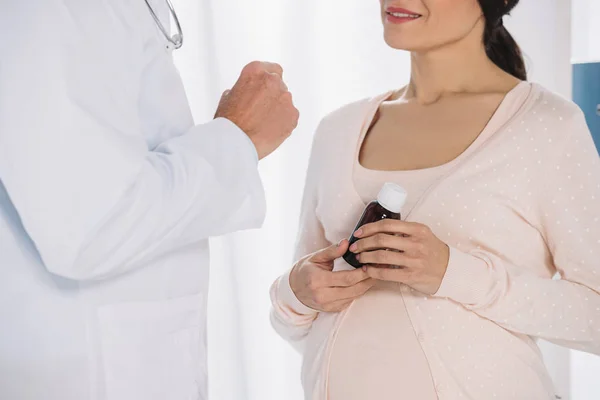 Immagine ritagliata di donna incinta in possesso di pillole e medico di ascolto — Foto stock
