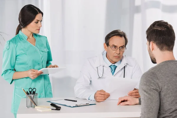 Médico hablando con el paciente y la enfermera que sostiene el comprimido - foto de stock
