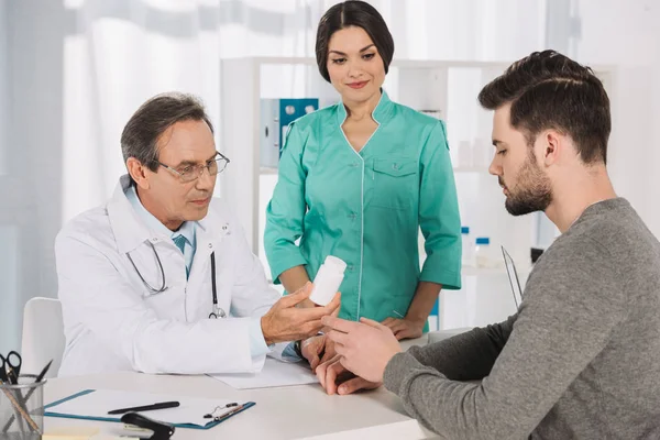 Doctor dando pastillas a joven hombre guapo - foto de stock