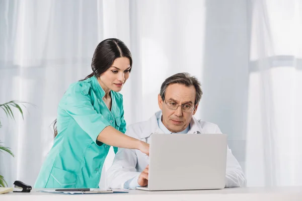 Enfermera mostrando algo en el ordenador portátil al médico - foto de stock