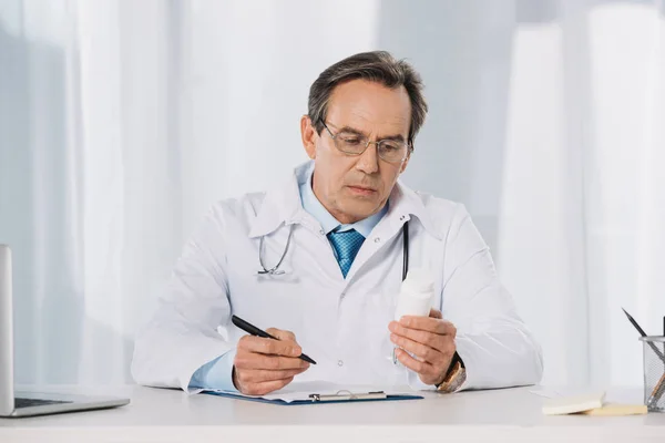 Médico sosteniendo pluma y mirando las píldoras - foto de stock
