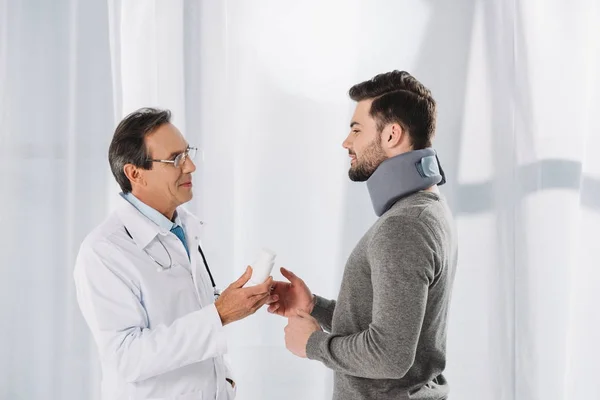 Médico dando píldoras al paciente con corsé en el cuello - foto de stock