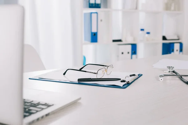 Brille und Stift auf Klemmbrett auf Arbeitstisch in Klinik — Stockfoto