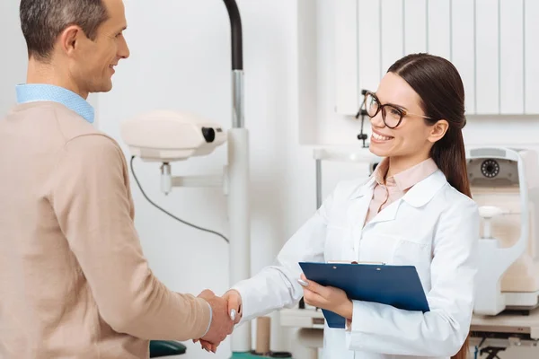 Side view of optometrist with notepad and patient shaking hands in hospital — Stock Photo