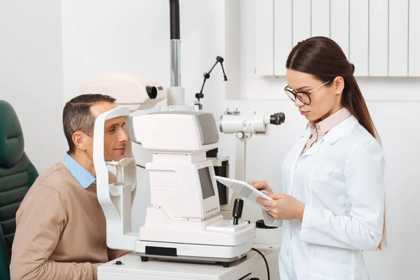 Vue latérale du patient obtenant examen oculaire dans la lampe à fente dans la clinique — Photo de stock