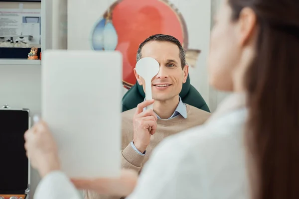 Selective focus of smiling man getting eye examination by oculist in clinic — Stock Photo