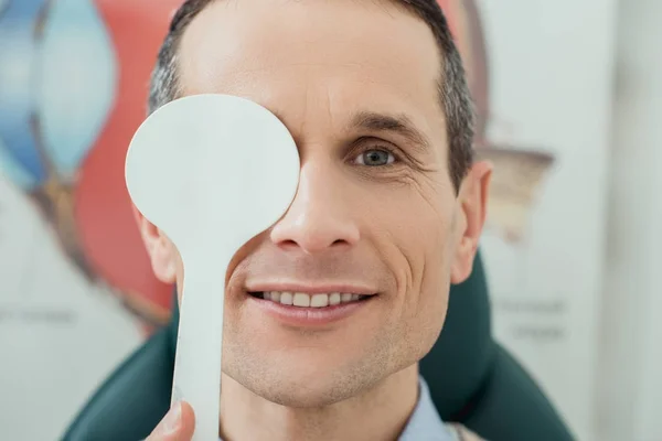 Obscured vista de sonriente hombre consiguiendo ojo prueba en clínica - foto de stock