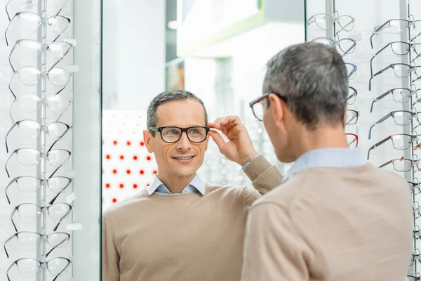 Souriant caucasien homme choisissant paire de lunettes en optique — Photo de stock