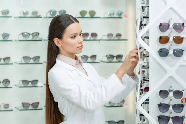 Side view of optometrist taking eyeglasses from shelf in optics — Stock Photo