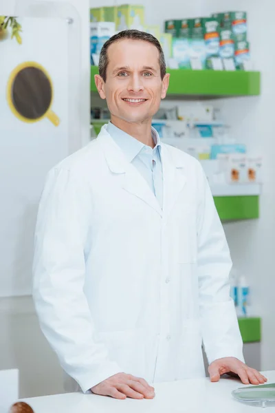 Портрет улыбающегося оптометриста в белом халате, стоящего у прилавка в оптике — стоковое фото