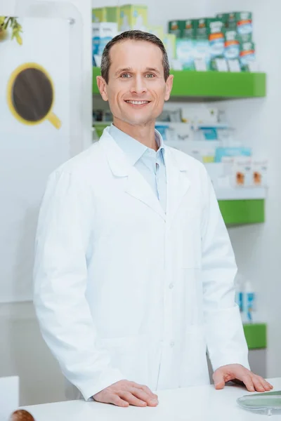 Porträt eines lächelnden Augenoptikers in weißem Mantel, der in Optik am Schalter steht — Stockfoto