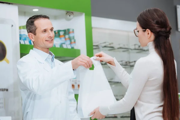 Oftalmologista sorrindo dando compra à mulher em óculos em óptica — Fotografia de Stock