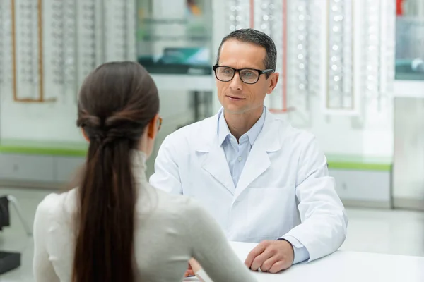 Selektiver Fokus der Seitenansicht des Augenarztes und der jungen Frau im Gespräch in der Optik — Stockfoto