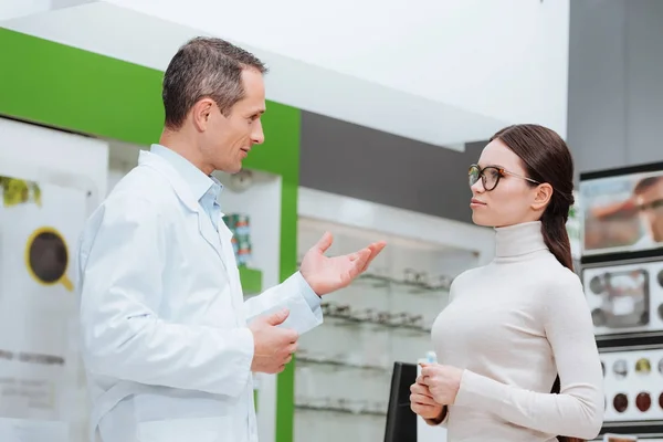 Side view of oculist and young woman having conversation in optics — Stock Photo