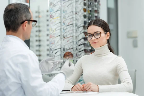 Partial view of optometrist showing lens to patient in optics — Stock Photo