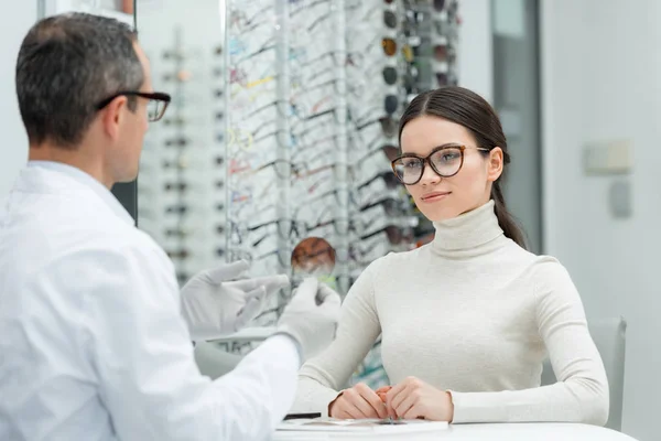 Visão parcial do optometrista mostrando lente ao paciente em óptica — Fotografia de Stock