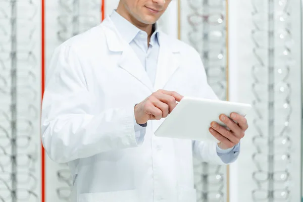 Cropped shot of oculist using tablet in optics with eyeglasses on shelves — Stock Photo