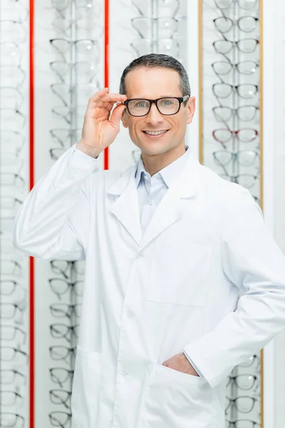 Portrait of smiling oculist in eyeglasses standing in optics — Stock Photo