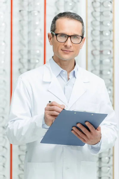 Portrait d'optométriste avec bloc-notes dans les mains regardant la caméra en optique — Photo de stock