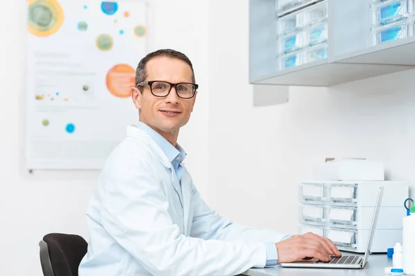 Side view of doctor in white coat working on laptop at workplace in clinic — Stock Photo