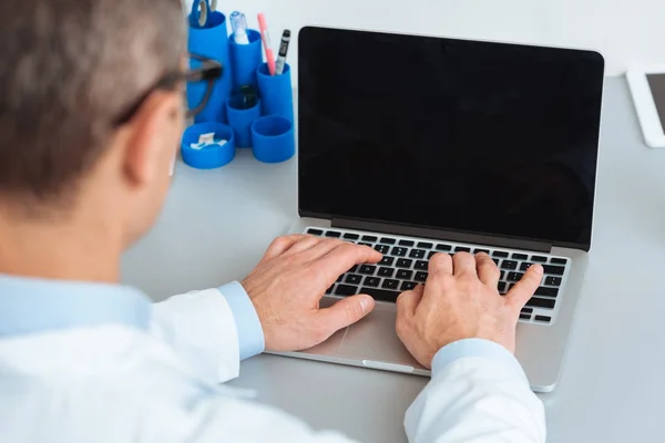 Partial view of doctor working on laptop with blank screen at table in clinic — Stock Photo