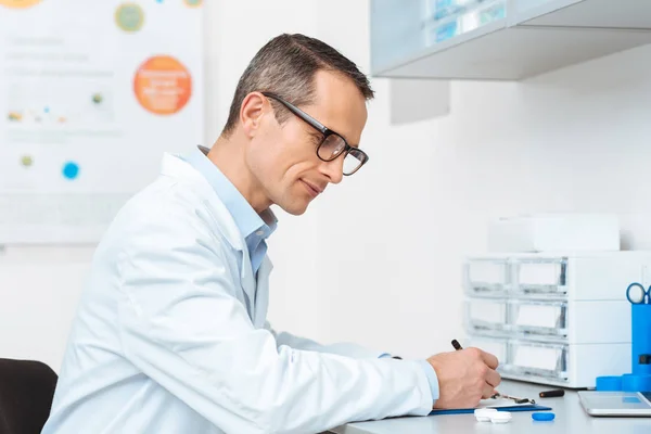 Vue latérale de l'ophtalmologiste travaillant à table en clinique — Photo de stock