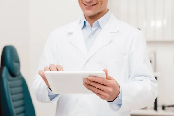 Vista parziale del medico sorridente in camice bianco con tablet digitale in clinica — Foto stock