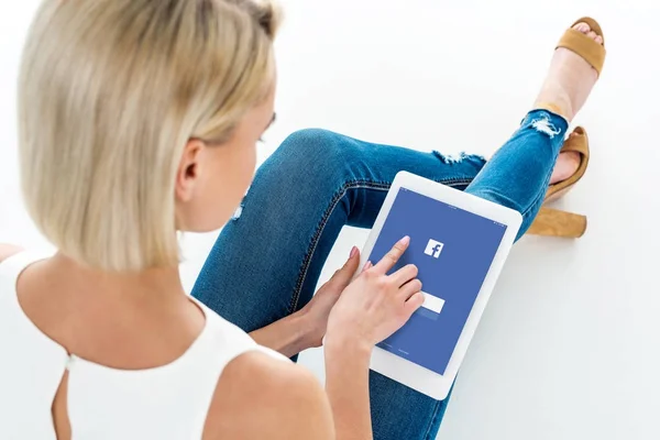 Вид сзади блондинки, использующей цифровой планшет с приложением Facebook, изолированный на белом — стоковое фото