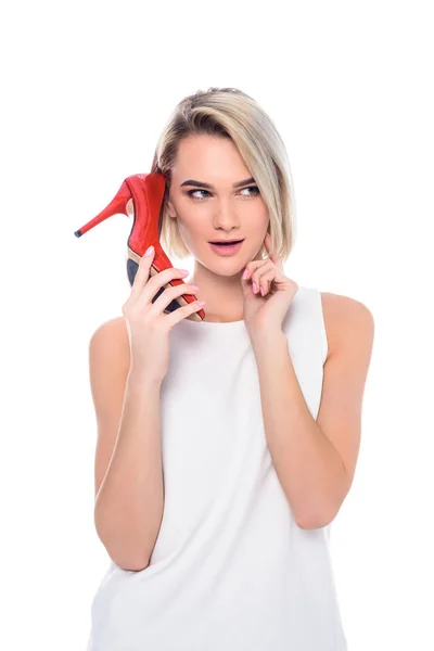 Приваблива кучерява жінка тримає взуття на каблуці як телефон, ізольована на білому — стокове фото