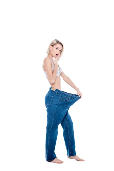 Shocked slim girl in old jeans old jeans after losing weight, isolated on white — Stock Photo