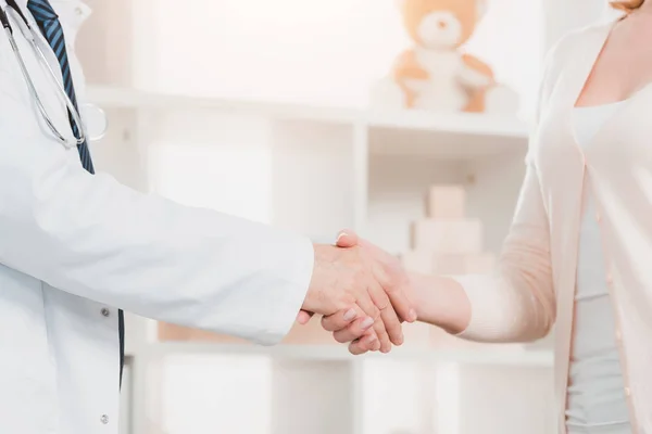Обрезанный снимок врача и пациента, пожимающего друг другу руки в клинике — стоковое фото