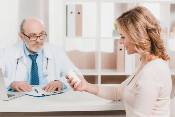 Selective focus of smiling woman looking at pills in hand in clinic — Stock Photo