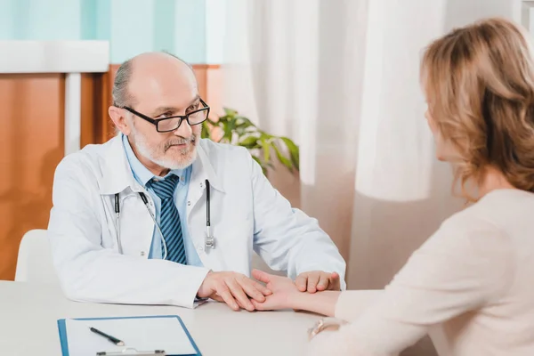 Partial view of senior doctor checking patients pulse at workplace in clinic — Stock Photo