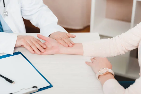 Colpo ritagliato del medico che controlla il polso dei pazienti sul posto di lavoro in clinica — Foto stock