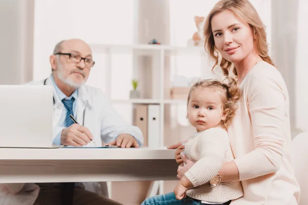 Mother and little daughter looking at camera during doctors reception in clinic — Stock Photo